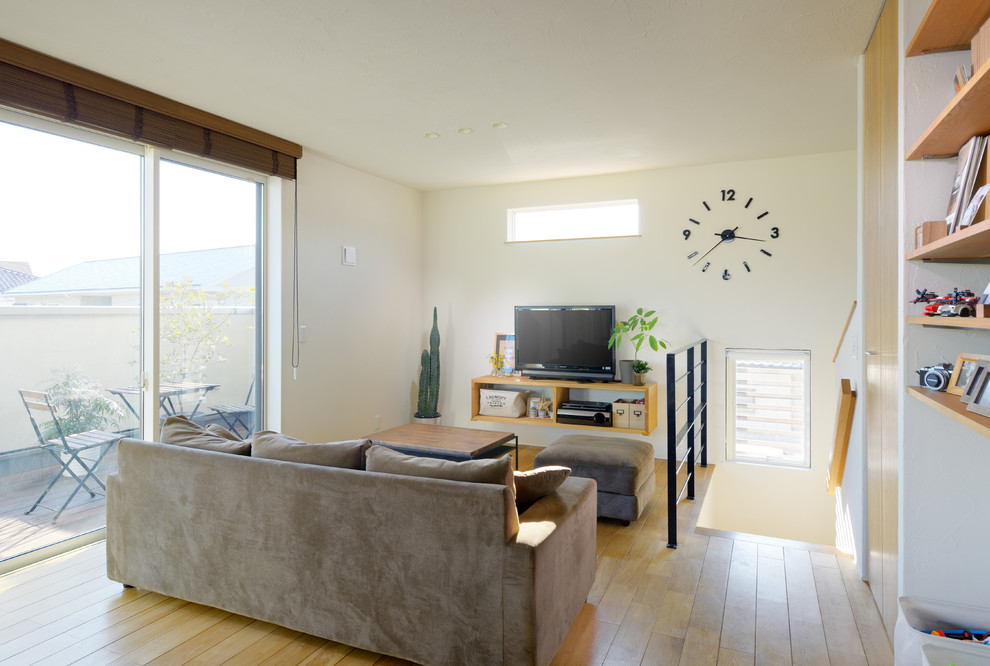 Пример оригинального дизайна: маленькая открытая гостиная комната в скандинавском стиле с белыми стенами, паркетным полом среднего тона, отдельно стоящим телевизором и коричневым полом для на участке и в саду
