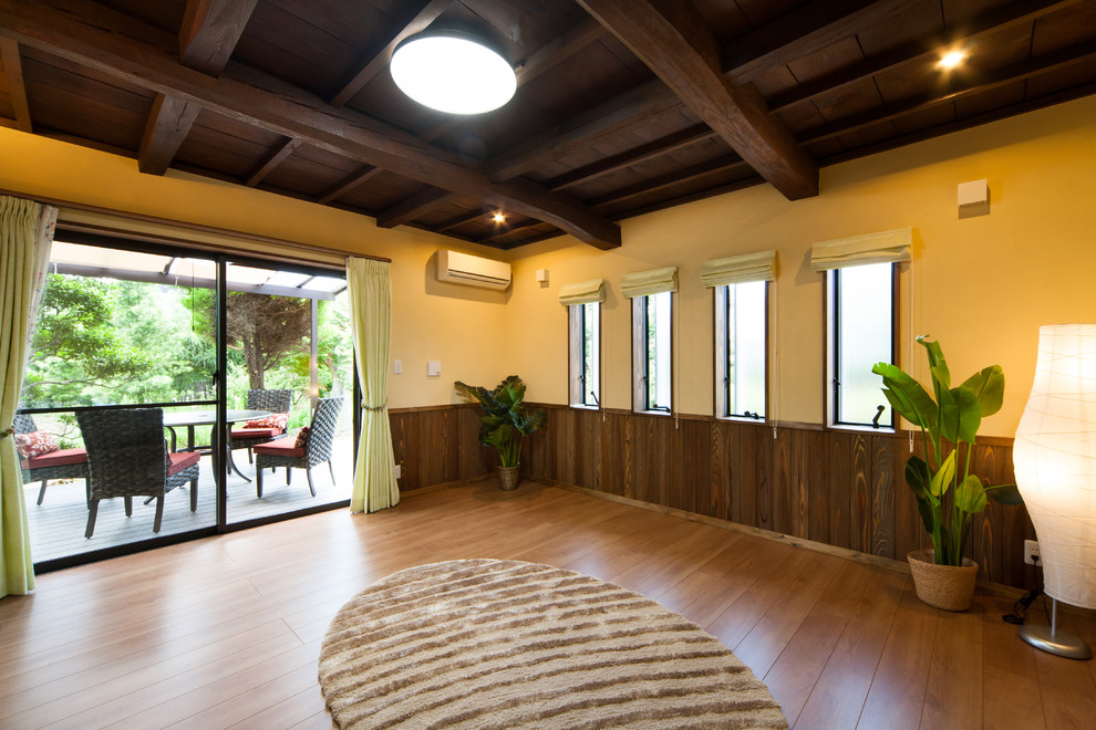 Cette image montre un salon asiatique avec un mur jaune, un sol en bois brun, un sol marron et un téléviseur indépendant.