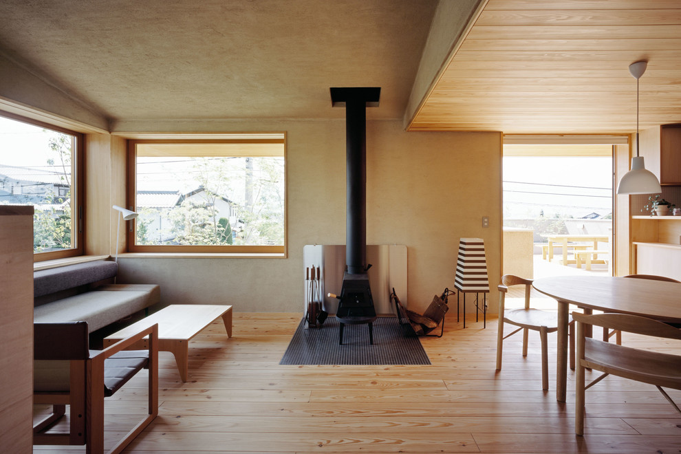 Imagen de salón abierto asiático con paredes beige, suelo de madera clara, estufa de leña y marco de chimenea de metal