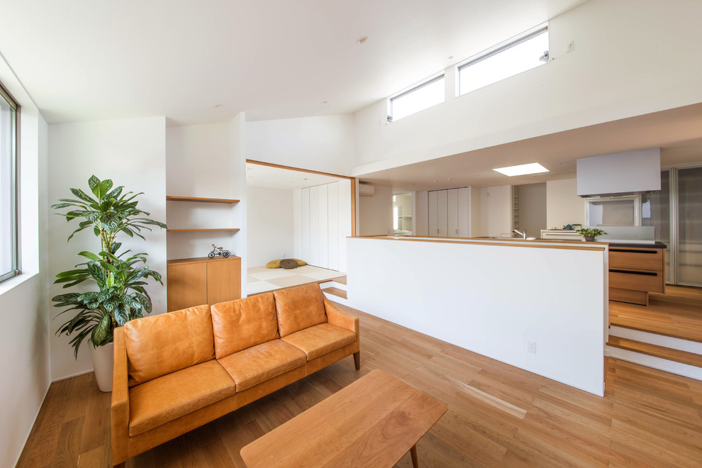 На фото: открытая гостиная комната в стиле модернизм с белыми стенами, полом из фанеры, отдельно стоящим телевизором и коричневым полом