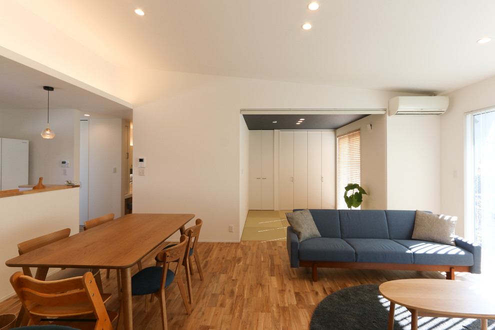 Cette image montre un salon design de taille moyenne et ouvert avec un mur blanc, un sol en bois brun, aucune cheminée et un sol marron.