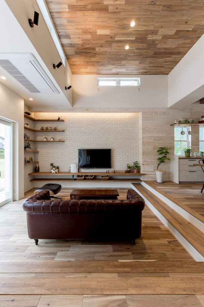 Foto di un grande soggiorno etnico aperto con pavimento in legno massello medio, pareti bianche, TV a parete, pavimento beige e pareti in legno