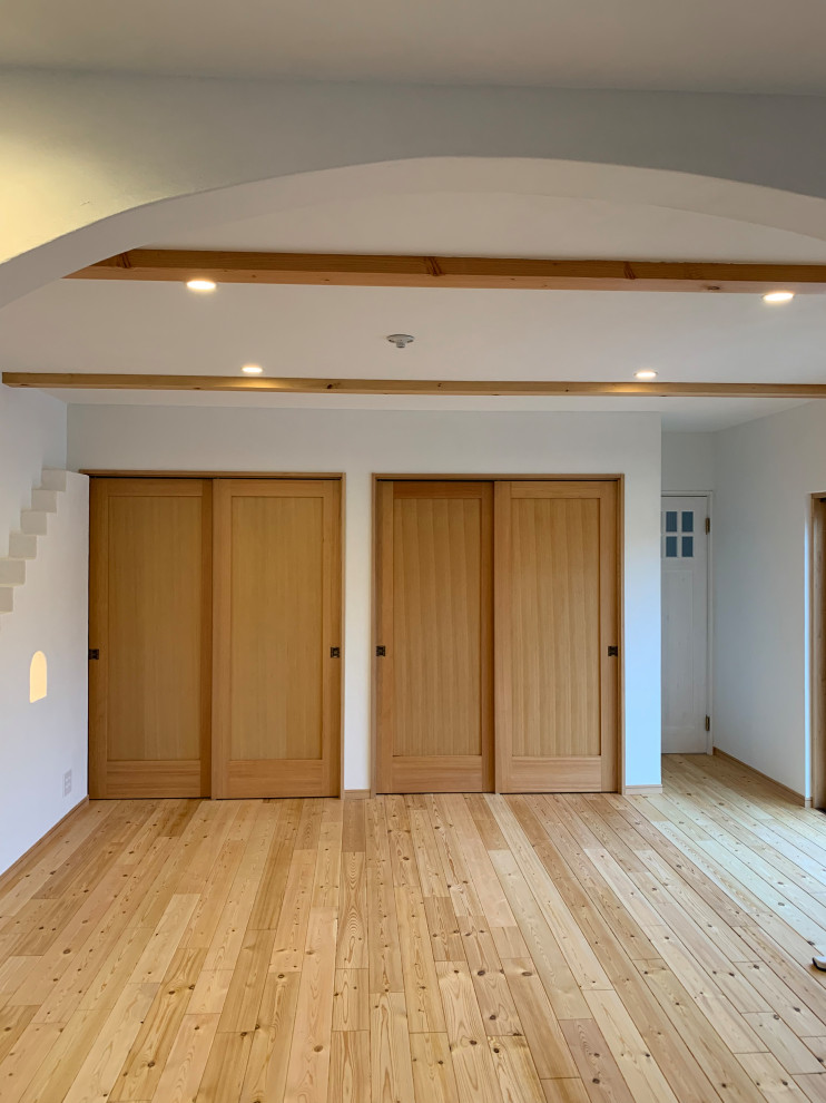Foto på ett amerikanskt vardagsrum, med vita väggar, ljust trägolv, TV i ett hörn och beiget golv