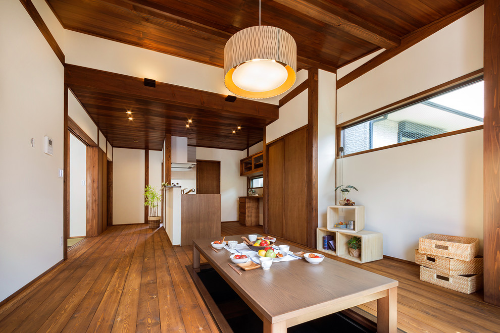 Imagen de salón abierto asiático con paredes blancas, suelo de madera en tonos medios y suelo marrón