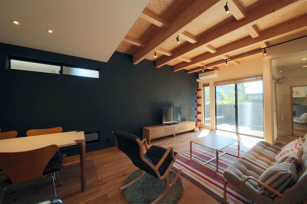 Стильный дизайн: маленькая гостиная комната в восточном стиле с черными стенами, отдельно стоящим телевизором, полом из фанеры и коричневым полом без камина для на участке и в саду - последний тренд