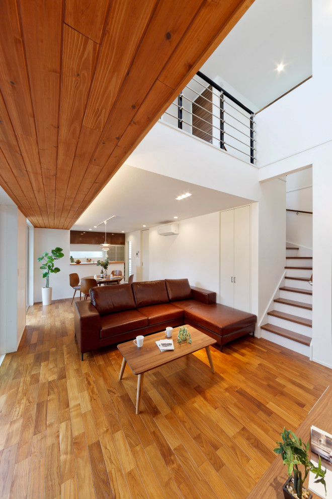 Offenes Wohnzimmer mit weißer Wandfarbe, braunem Holzboden, TV-Wand, braunem Boden, Tapetendecke und Holzdielenwänden in Sonstige