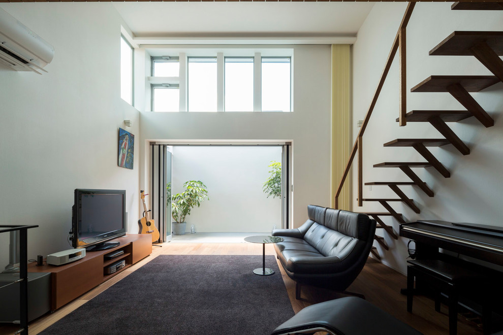 This is an example of a contemporary living room in Tokyo with white walls, light hardwood flooring, a freestanding tv and brown floors.