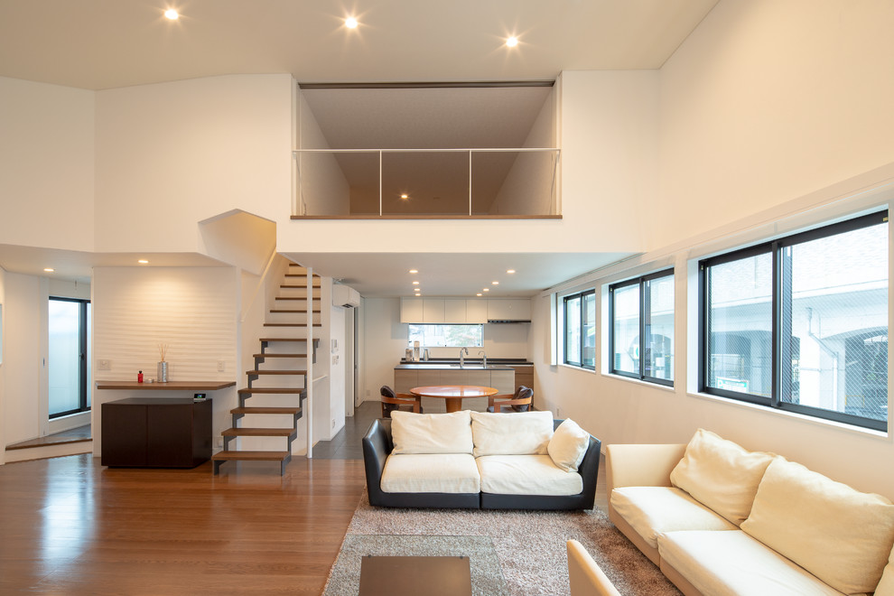 Идея дизайна: большая открытая гостиная комната в стиле модернизм с белыми стенами, светлым паркетным полом, отдельно стоящим телевизором и коричневым полом