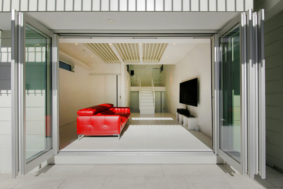 Diseño de salón abierto minimalista grande con paredes blancas, suelo de baldosas de cerámica, televisor colgado en la pared y suelo blanco