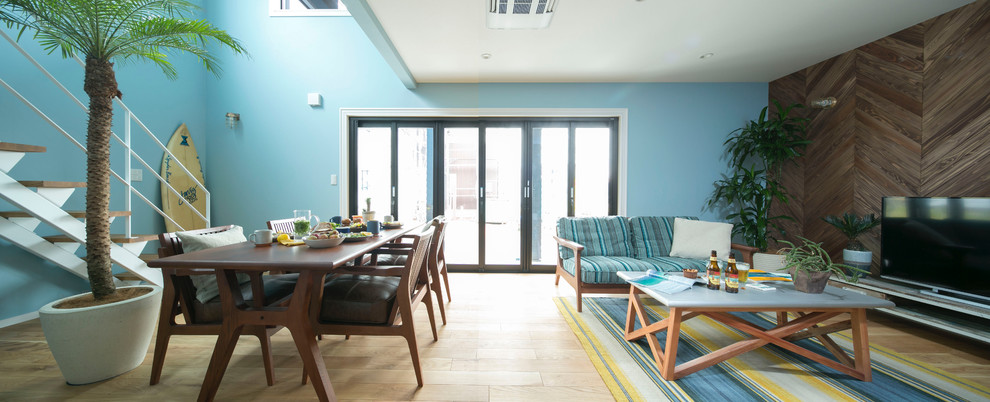 Ejemplo de salón abierto costero con paredes azules, suelo de madera clara y televisor independiente