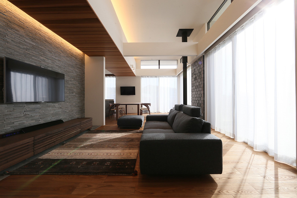 Immagine di un soggiorno minimal aperto con pareti grigie, pavimento in legno massello medio, stufa a legna, cornice del camino in mattoni e TV a parete