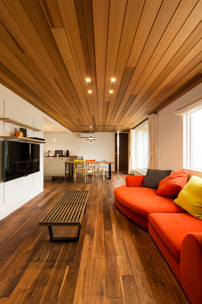 Imagen de salón abierto moderno con paredes blancas, suelo de madera oscura, televisor colgado en la pared y suelo marrón