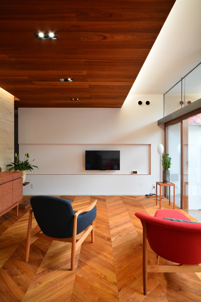 Modelo de salón abierto de estilo zen sin chimenea con paredes blancas, suelo de madera en tonos medios, televisor colgado en la pared y suelo marrón
