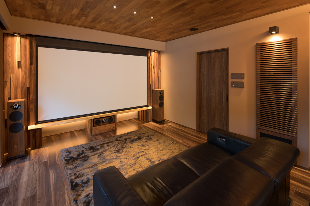 Cette photo montre une salle de cinéma tendance avec un mur beige, un sol en bois brun, un écran de projection et un sol marron.