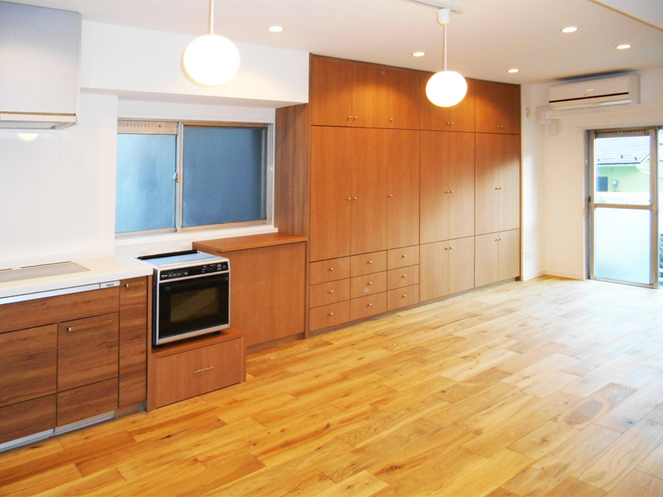 Modern open plan living room in Tokyo with light hardwood flooring and brown walls.