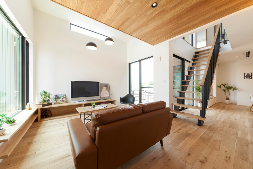 Modernes Wohnzimmer mit weißer Wandfarbe, hellem Holzboden, freistehendem TV und beigem Boden in Sonstige