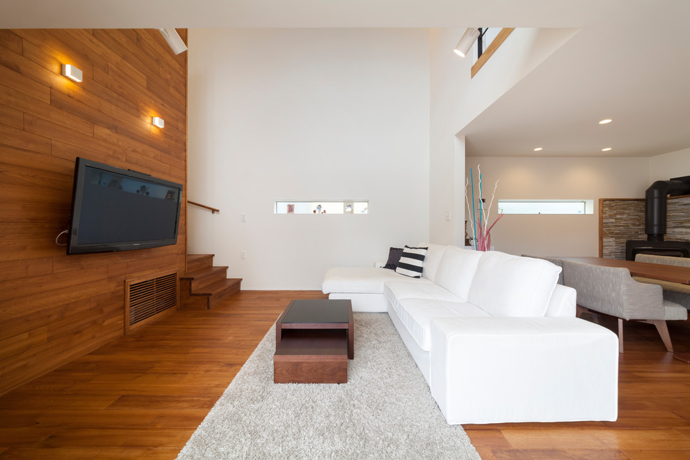 Modelo de salón minimalista con paredes blancas, televisor colgado en la pared y suelo marrón