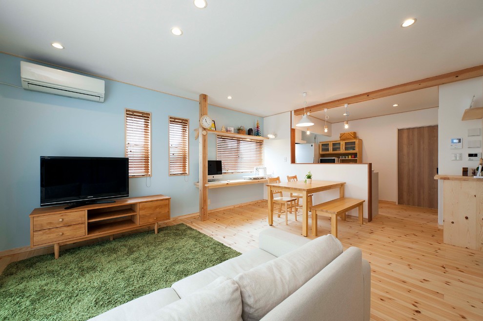 Diseño de salón de estilo zen con paredes azules, suelo de madera clara, televisor independiente y suelo marrón