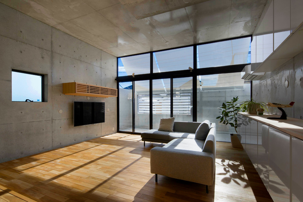 Inredning av ett modernt vardagsrum, med grå väggar, ljust trägolv, en väggmonterad TV och brunt golv