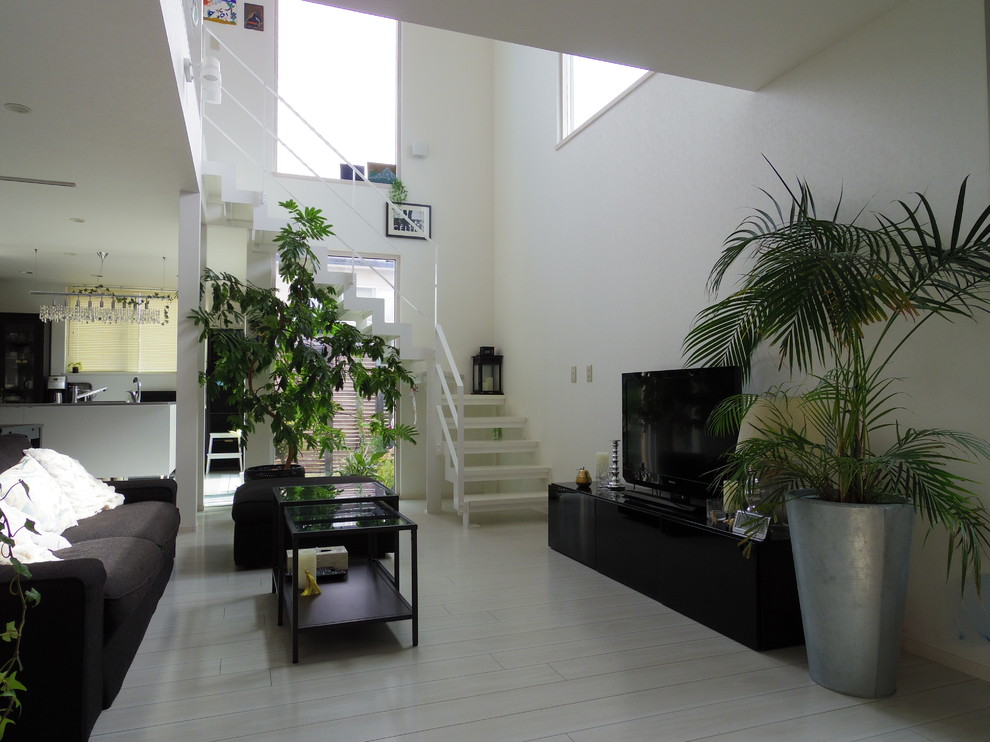 Offenes Modernes Wohnzimmer mit weißer Wandfarbe, freistehendem TV, Sperrholzboden und grauem Boden in Sonstige
