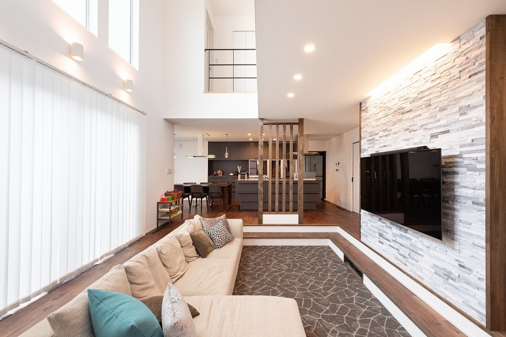 Bild på ett funkis allrum med öppen planlösning, med vita väggar, mörkt trägolv, en väggmonterad TV och brunt golv