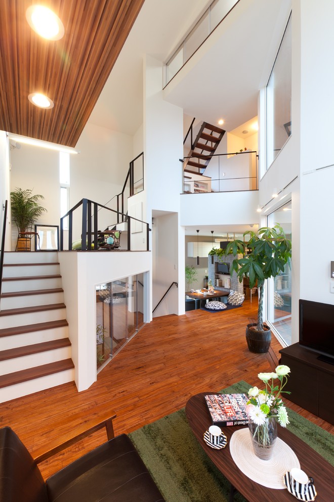Offenes Modernes Wohnzimmer mit weißer Wandfarbe, braunem Holzboden, freistehendem TV und braunem Boden in Sonstige