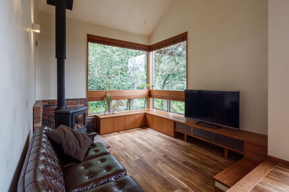 Modelo de salón abierto asiático con paredes blancas, suelo de madera oscura, televisor independiente, suelo marrón y estufa de leña