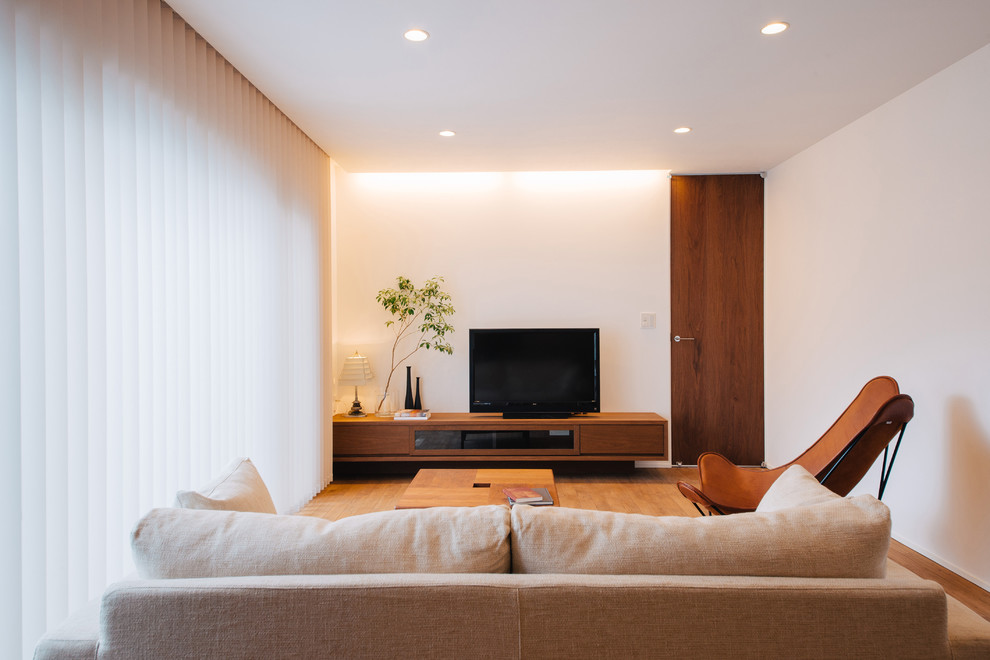 Modern inredning av ett allrum med öppen planlösning, med vita väggar, mellanmörkt trägolv och en fristående TV