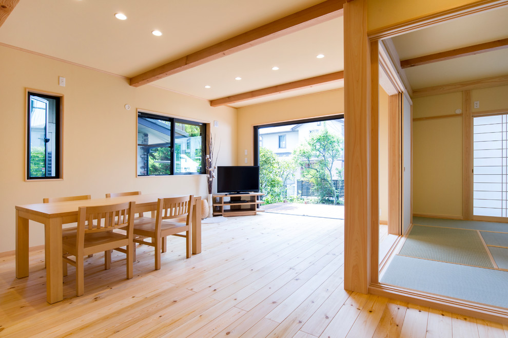 Modelo de salón abierto de estilo zen con paredes blancas, suelo de madera clara, televisor independiente y suelo beige