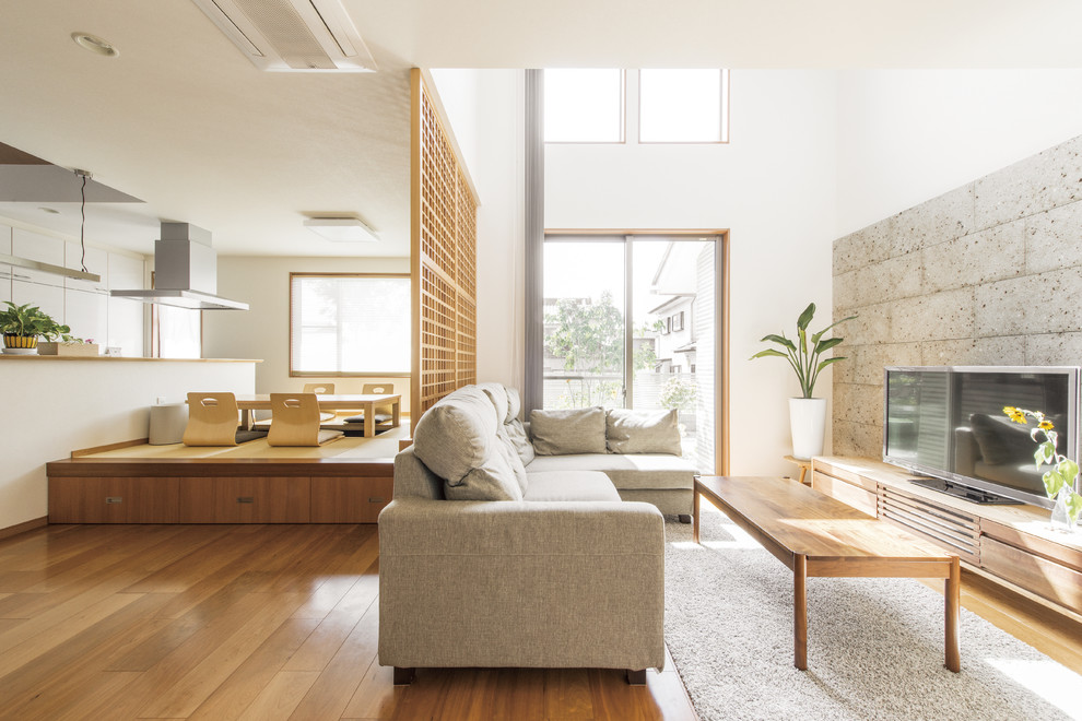 Modelo de salón abierto de estilo zen con paredes blancas, suelo de madera en tonos medios, televisor independiente y suelo marrón