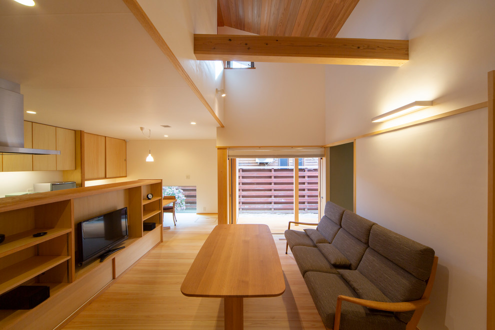 Offenes Nordisches Wohnzimmer mit weißer Wandfarbe, braunem Holzboden, freistehendem TV und braunem Boden in Sonstige
