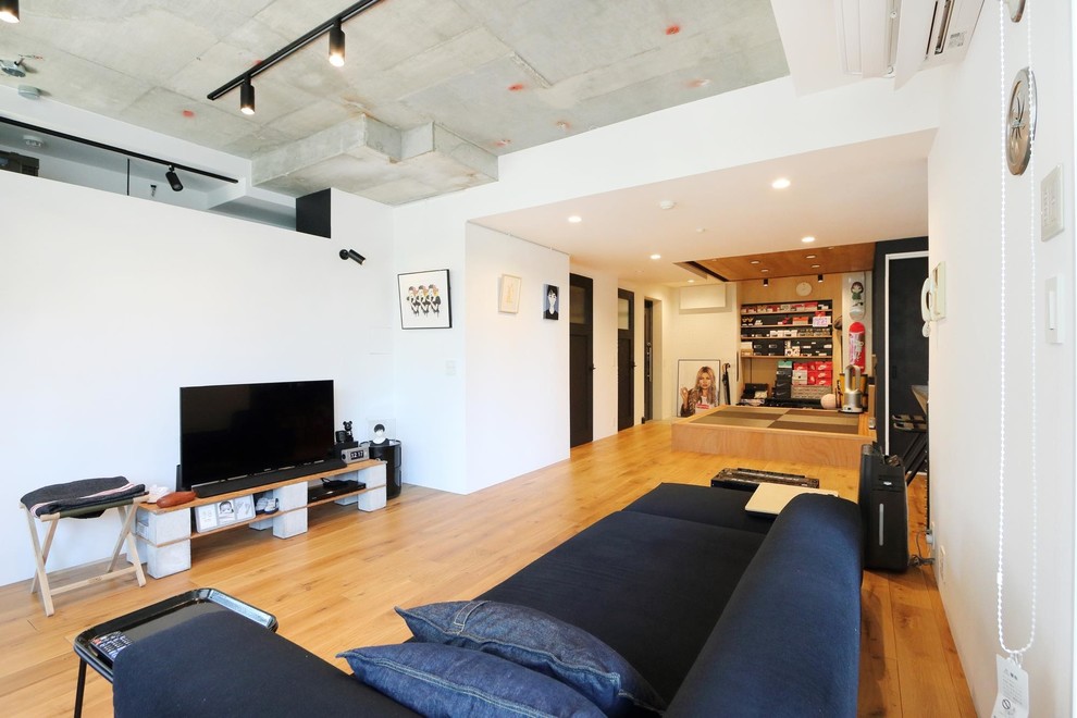 Cette photo montre un salon industriel ouvert avec un mur blanc, un sol en bois brun, un téléviseur indépendant et un sol marron.