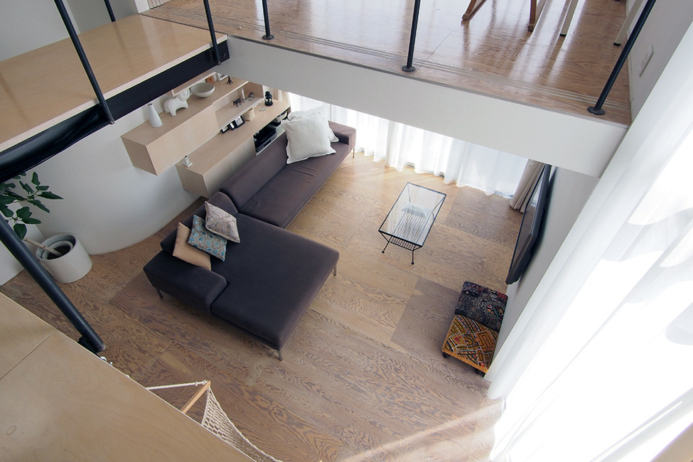 На фото: открытая гостиная комната среднего размера в стиле модернизм с белыми стенами, полом из фанеры и телевизором на стене без камина