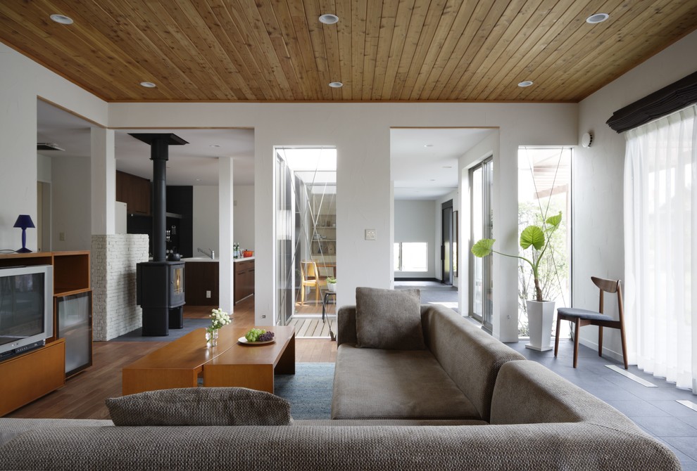 Пример оригинального дизайна: открытая гостиная комната в стиле модернизм с белыми стенами, печью-буржуйкой, отдельно стоящим телевизором и фасадом камина из кирпича