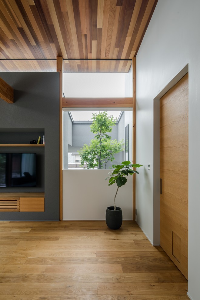 Modelo de salón abierto asiático grande con paredes grises, suelo de madera en tonos medios, televisor colgado en la pared y suelo marrón