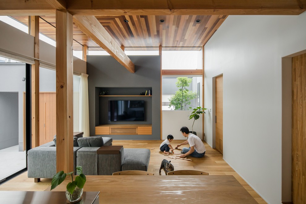 Großes, Offenes Asiatisches Wohnzimmer mit grauer Wandfarbe, braunem Holzboden, TV-Wand und braunem Boden in Sonstige