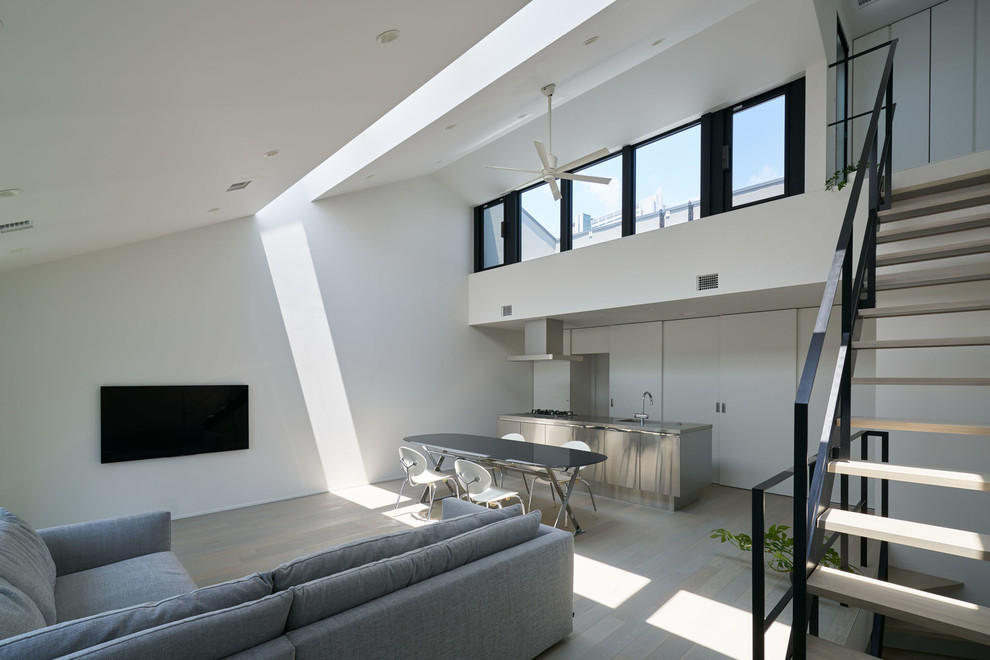 This is an example of a medium sized modern open plan living room in Tokyo with white walls, plywood flooring, a wall mounted tv and grey floors.