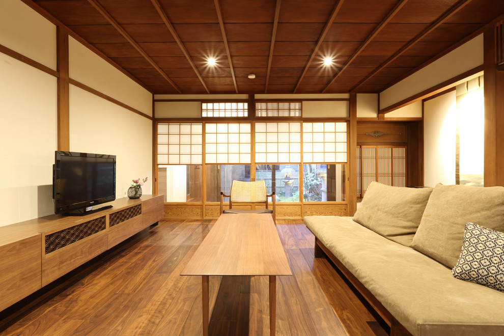 Inredning av ett asiatiskt mellanstort allrum med öppen planlösning, med vita väggar, mörkt trägolv, en fristående TV och brunt golv