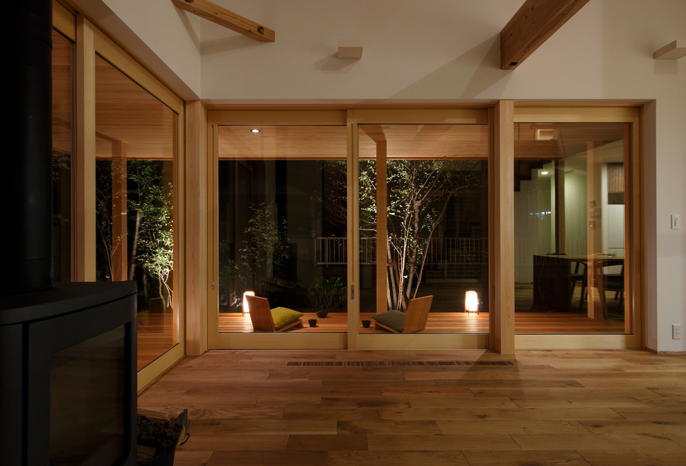 Fernseherloses Asiatisches Wohnzimmer mit weißer Wandfarbe, braunem Holzboden und Kaminofen in Sonstige