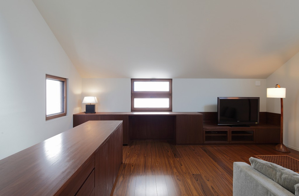 Small modern enclosed living room in Tokyo with a reading nook, white walls, plywood flooring, no fireplace, a brick fireplace surround, a freestanding tv, brown floors and a vaulted ceiling.