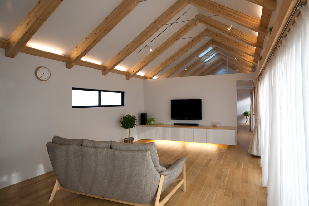 На фото: открытая гостиная комната среднего размера в скандинавском стиле с белыми стенами, полом из фанеры и телевизором на стене