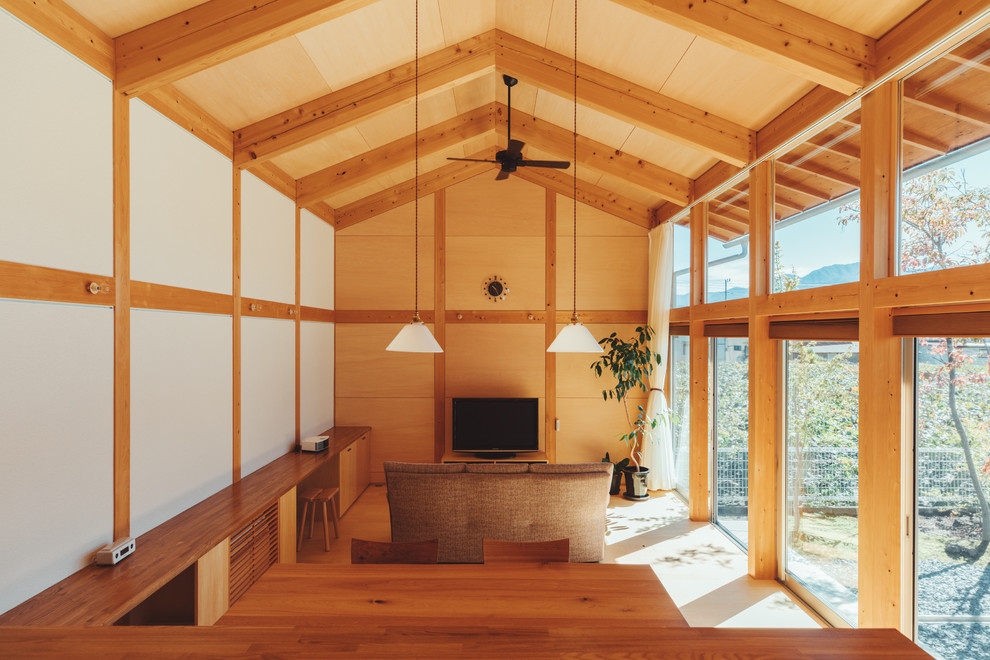 Offenes Asiatisches Wohnzimmer mit bunten Wänden, hellem Holzboden, freistehendem TV und braunem Boden in Sonstige