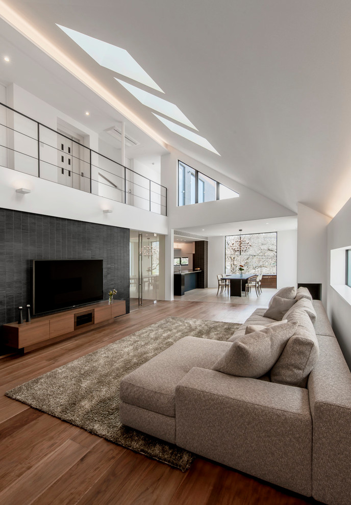 Пример оригинального дизайна: открытая гостиная комната в современном стиле с белыми стенами, паркетным полом среднего тона, коричневым полом и телевизором на стене