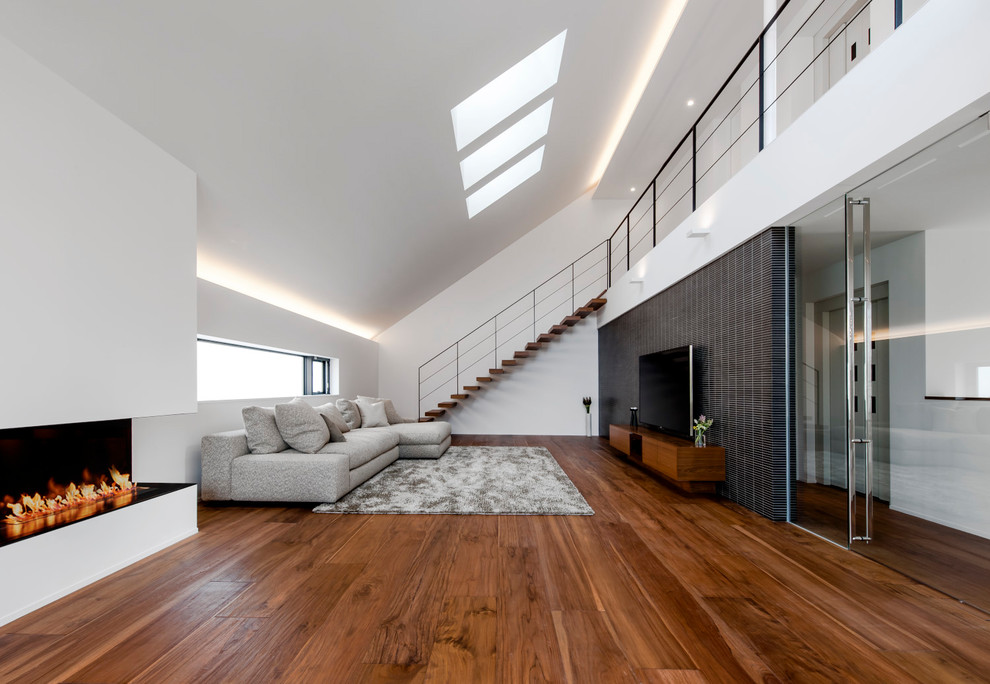 Imagen de salón cerrado contemporáneo con paredes blancas, suelo de madera en tonos medios, chimenea lineal y suelo marrón