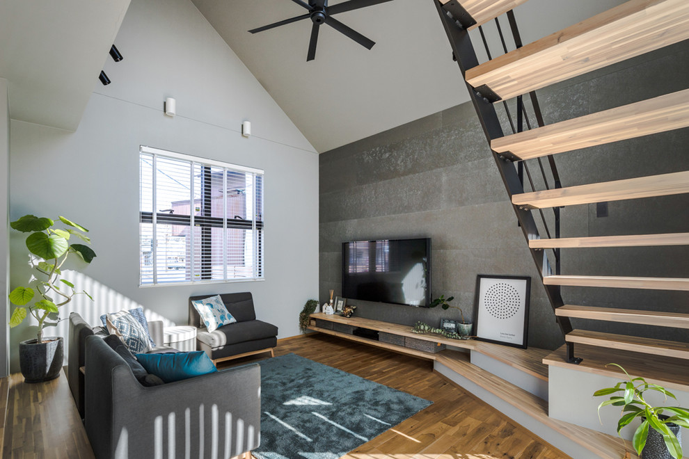 Immagine di un soggiorno nordico di medie dimensioni e aperto con pareti grigie, pavimento in legno massello medio, TV a parete e pavimento marrone