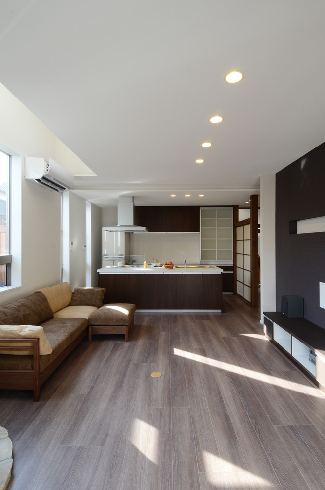 Bild på ett funkis allrum med öppen planlösning, med vita väggar, plywoodgolv, en öppen vedspis, en spiselkrans i sten, en väggmonterad TV och brunt golv
