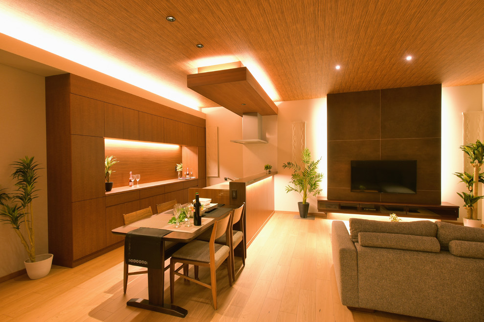 Inredning av ett asiatiskt allrum med öppen planlösning, med vita väggar, ljust trägolv, en väggmonterad TV och brunt golv
