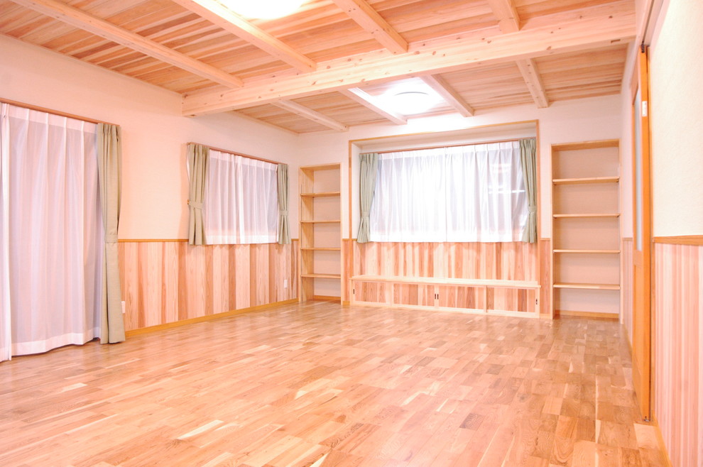 Cette image montre un grand salon asiatique ouvert avec une salle de réception, un mur beige, un sol en bois brun, aucune cheminée, un téléviseur fixé au mur et un sol beige.