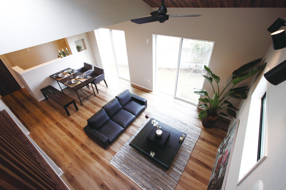 Imagen de salón abierto actual con paredes blancas, suelo de contrachapado y suelo marrón