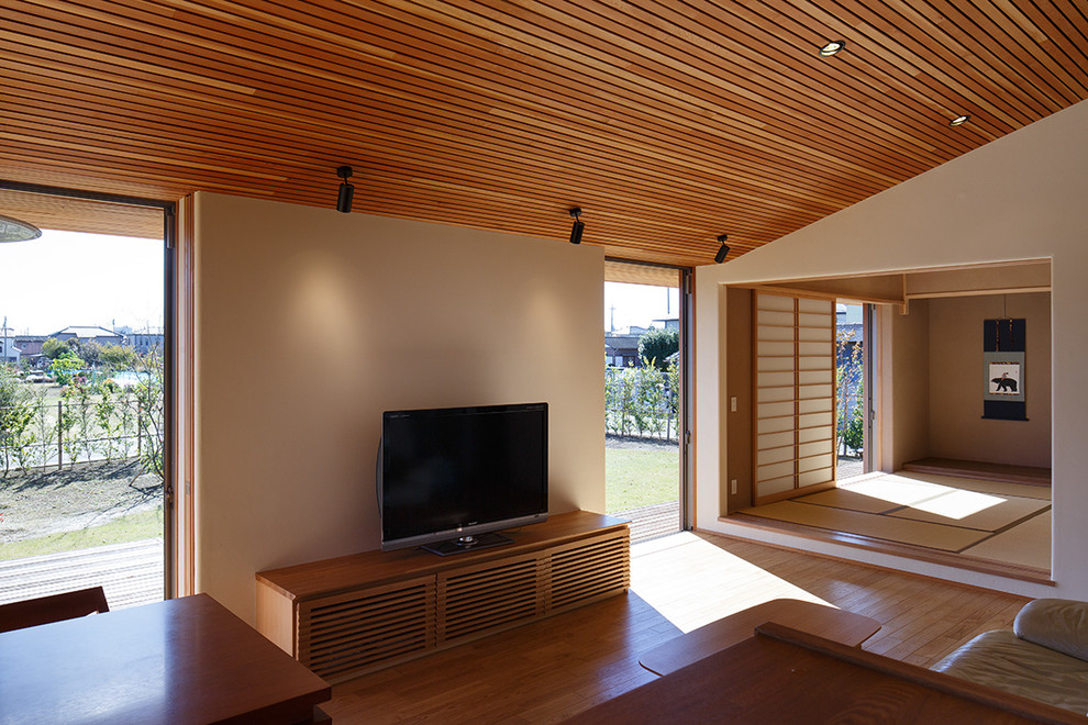 Foto på ett mellanstort orientaliskt allrum med öppen planlösning, med vita väggar, mellanmörkt trägolv, en fristående TV och brunt golv